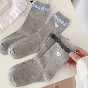 Detail of grey ruffled crew socks featuring decorative white heart buttons and knit texture