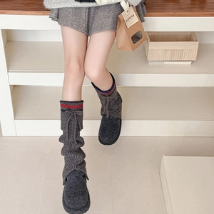 Close-up of dark grey knitted leg warmers featuring red-blue stripes and tied ribbon bows