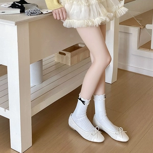 Detail of white ruffle crew socks with black bows paired with ballet flat shoes
