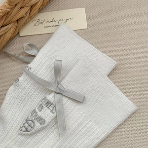 Detail of white ribbed socks featuring a dark grey satin bow and embroidered text detail