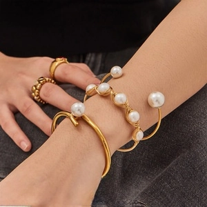 Detail of multi-layered gold pearl wrap bracelet and open cuff on model's wrist