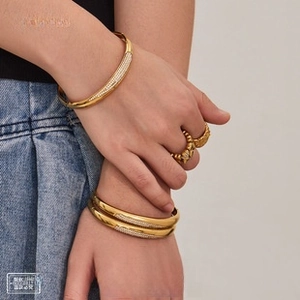 Macro detail of 18K gold plated wide bangles with pavé zircon and vintage textured rings
