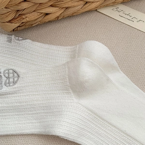 Detail of white ribbed crew socks featuring heart embroidery and bow on the heel