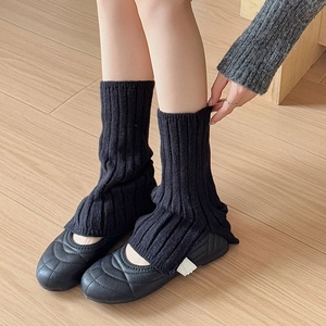 Close-up of black ribbed knit leg warmers paired with quilted flat shoes on wood floor