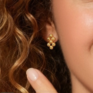 Macro detail of stacked gold beaded earrings worn to show elegant metallic texture