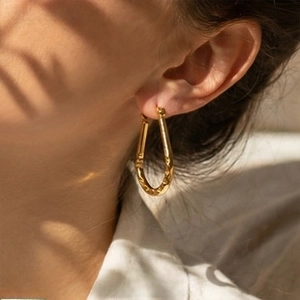 Detailed close-up of a gold U-shaped textured earring with liquid metal aesthetic on a model