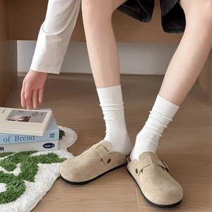 Détail de sabots en daim beige avec boucle en métal réglable et chaussettes tricotées