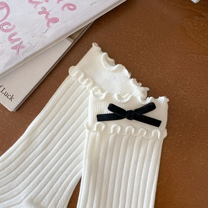 Detail of white cotton socks with ruffled edges and black velvet bow on wood