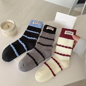 Three pairs of striped mid-calf socks with cute patches and ruffled textures on a desk