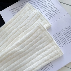 Detail of white ribbed knit leg warmers showing thick texture on vintage book background