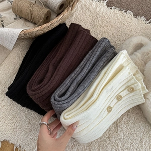 Close-up of ribbed knit leg warmers in neutral colors featuring side button details