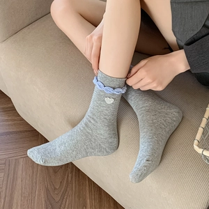 Detail of grey knit sock with light blue ruffle trim and a white heart button accent