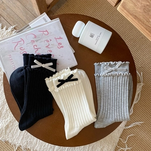 Close-up of three pairs of ruffled socks with velvet bows in black, white, and grey