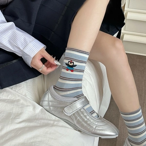 Détail de chaussettes rayées bleues avec broderie pingouin et chaussures plates argentées