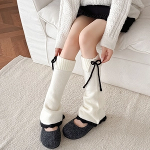 Détail de jambières en tricot blanc avec nœud noir et ourlet en dentelle contrastée