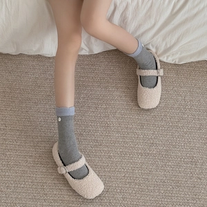 Close-up of cream fuzzy Mary Jane flats with metal buckles and gray knit socks