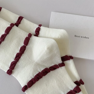 Close-up of cream knit socks featuring burgundy 3D wavy stripes and ribbed texture