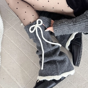 Détail de jambières en tricot gris avec nœud blanc et bordure à volants