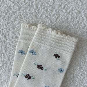 Gros plan détaillé de chaussettes en maille crème avec fleurs bleues et bords ondulés