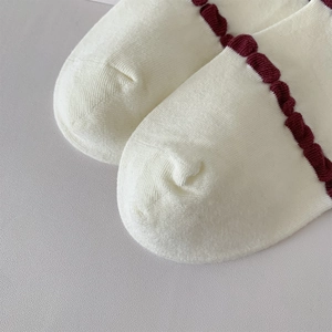 Detail shot of white cotton socks featuring a delicate burgundy ruffled edge and soft texture