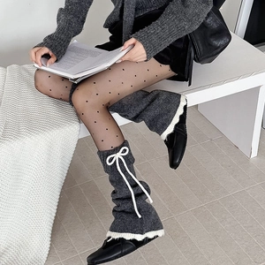 Détail de jambières en tricot gris avec bordure blanche à volants et nœuds décoratifs