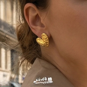 Detail shot of heart-shaped gold earrings with textured surface worn by a model