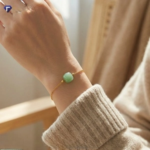Detail of 18K gold chain bracelet with square green gemstone worn on female wrist