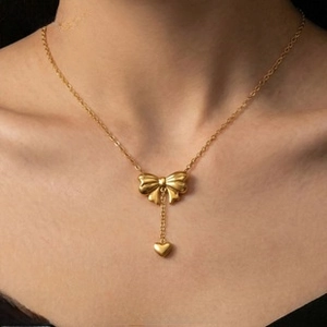 Close-up of golden stainless steel necklace with a bow knot and heart pendant detail
