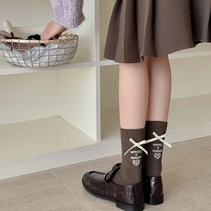 Close-up of brown knit sock with white silk bow and happiness lettering embroidery