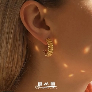 Close-up of golden ribbed C-shaped earrings worn by a model with elegant soft lighting