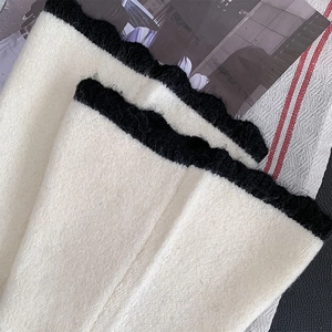 Gros plan de jambières en tricot crème avec bords festonnés noirs et texture moelleuse