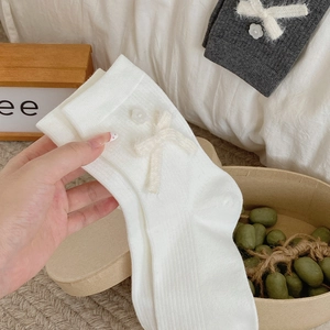 Detail of ribbed mid-calf socks with plush bows and pearl accents in white and grey