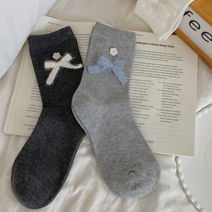 Detail of knit socks featuring plush bows and pearl flower accents on ribbed fabric