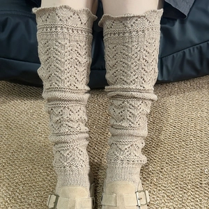 Close-up of beige pointelle knit leg warmers with floral lace pattern and scalloped edges