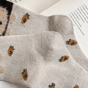 Gros plan de chaussettes en maille beige avec motifs ours et carotte sur magazine