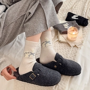 Close-up of rabbit pattern jacquard socks paired with grey felt clogs in a cozy setting