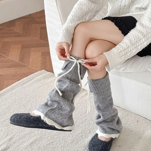 Jambières en tricot gris avec nœuds blancs et bordure en peluche dans un décor chaleureux