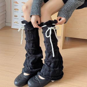 Close-up of black knit leg warmers with star patterns and white ribbon bows
