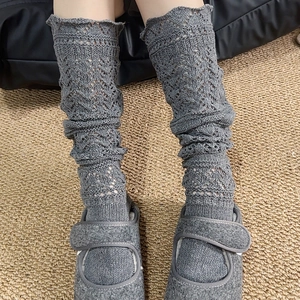 Detailed close-up of grey hollow-out knit leg warmers with delicate scalloped edges