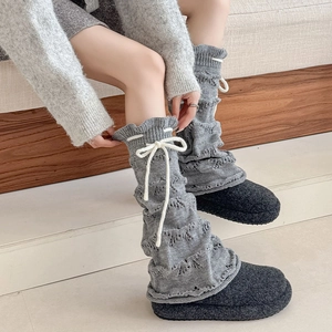 Detail of grey knitted leg warmers with white bow drawstring and wave texture