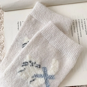 Detail view of cozy knit socks featuring a cute cartoon cat embroidery on cream fabric