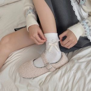 Detail of white knit socks with bow and floral accents paired with fuzzy Mary Jane shoes