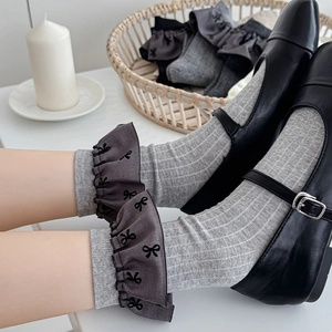 Detail von hellgrauen Rippsocken mit dunkelgrauen Rüschenbündchen und schwarzen Schleifen
