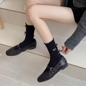 Dettaglio di calze nere con fiocco ricamo MD e bordo a balze con scarpe Mary Jane