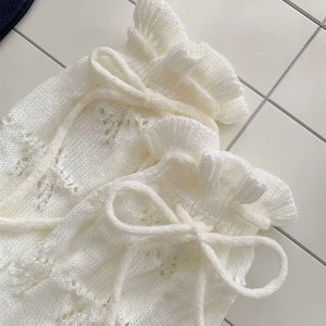 Detail of white knit leg warmer featuring hollow crochet ruffles and a delicate bow tie
