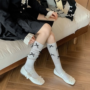 Detail of white rib-knit over-knee socks with black bow and Mary Jane shoes