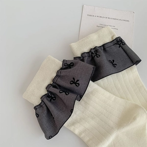Detail von cremeweißen Rippsocken mit grauer Chiffonspitze und schwarzem Schleifendruck