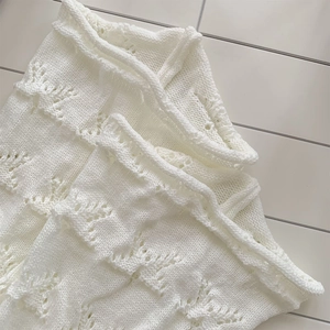 Close-up of white hollow knit fabric with delicate wavy patterns and soft texture