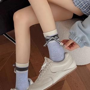Detail of light blue collegiate style mid-calf socks with a checkered bow and handmade label