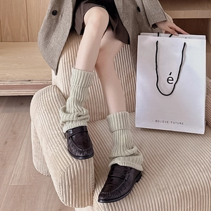Detail of beige ribbed knit leg warmers styled with black loafers for a cozy look
